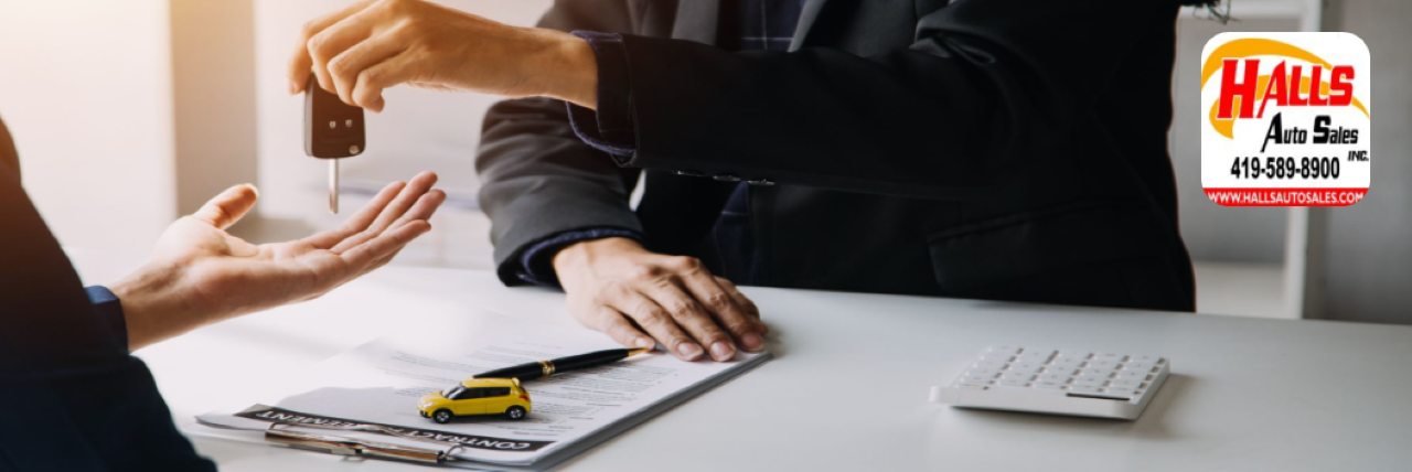 Happy customers taking keys to their newly purchased used car at Hall’s Auto Sales.